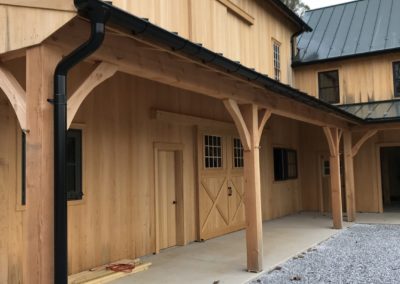 Barn porch roof with sliding stable doors. Black Nordic gutters and downspouts tying into underground pipes.