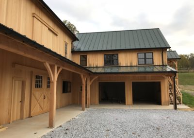 View of the barns inner corner. 2 utility vehicle garage, open doorways. Black gutters and downspouts.