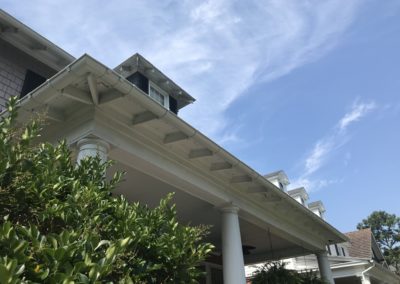 White gutters on a front porch. Green bushes and white columns.