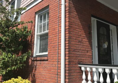 White downspout on red brick wall. Tied into an undergound pipe.