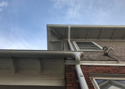 White gutters and downspouts on a shake and brick facade.
