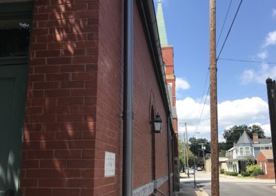 Red brick church side. Sidewalk. Anthracite metallic downspouts connecting into the underground pipes in the sidewalk.
