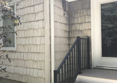 Stairs out to the gravel. Leaf chute going into a white underground pipe. White downspout.