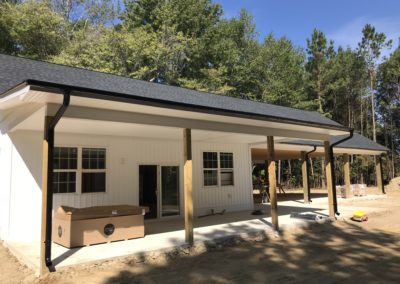 Bigger new workshop building in the country. Black gutters and downspouts. White siding and dark gray shingle roof.