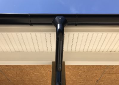 Black outlet from the gutter. Smooth elbows connecting down. OSB in the ceiling is exposed behind.