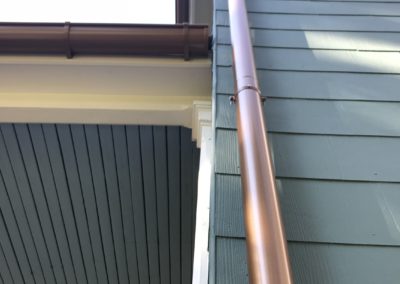 20 foot copper metallic downspout. Green siding and white trim. Seamless overlap between the dowsnpouts.