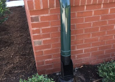 Black leaf chute connects to the groundpipe. Green downspout on the red brick water table.