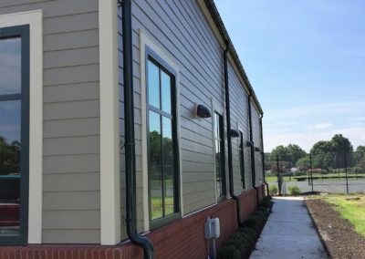 Dark green gutters and downspouts on beige siding. Red brick water table.