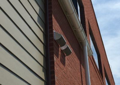 White gutters on beige siding and red brick wall.
